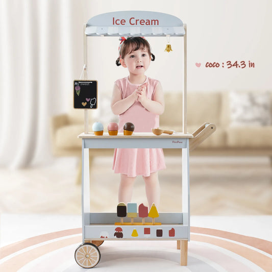 Happy toddler girl playing with a wooden ice cream stand. This pretend play kids toy features an awning, a ringing bell, and play food desserts.