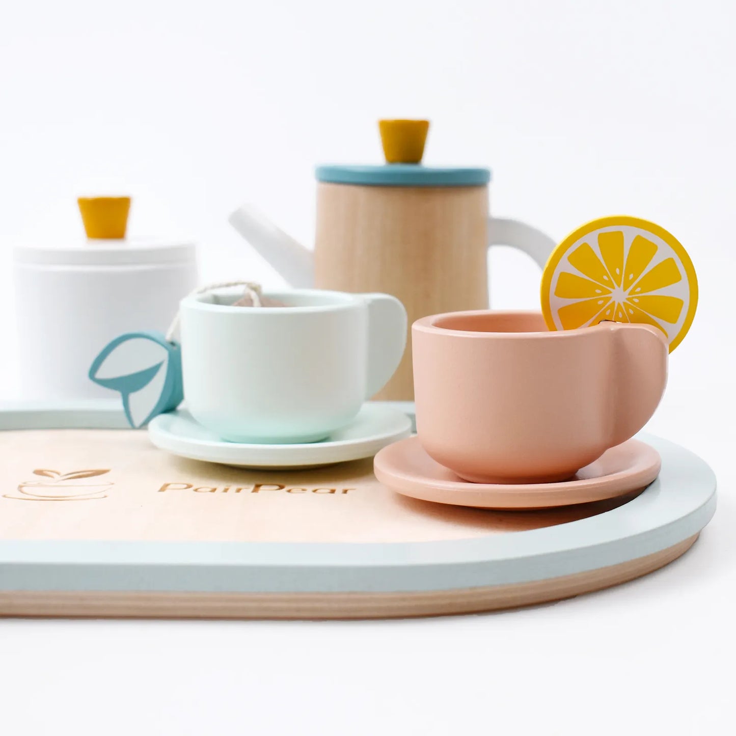 Close-up of the wooden pretend play tea set. Detailed pink and mint teacups with toy tea bags and attachable lemon slices for kids tea parties.
