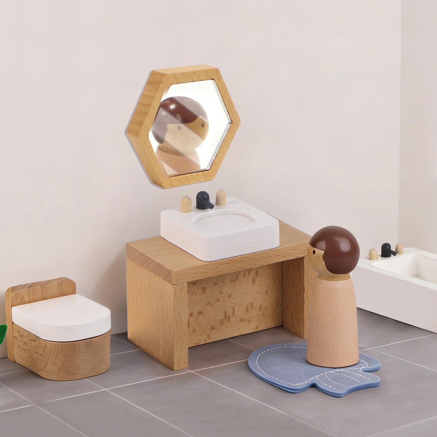 Miniature bathroom set from the wooden dollhouse furniture kit. Features a wooden bathtub, sink with a mirror, toilet, and a peg doll on a bath mat.