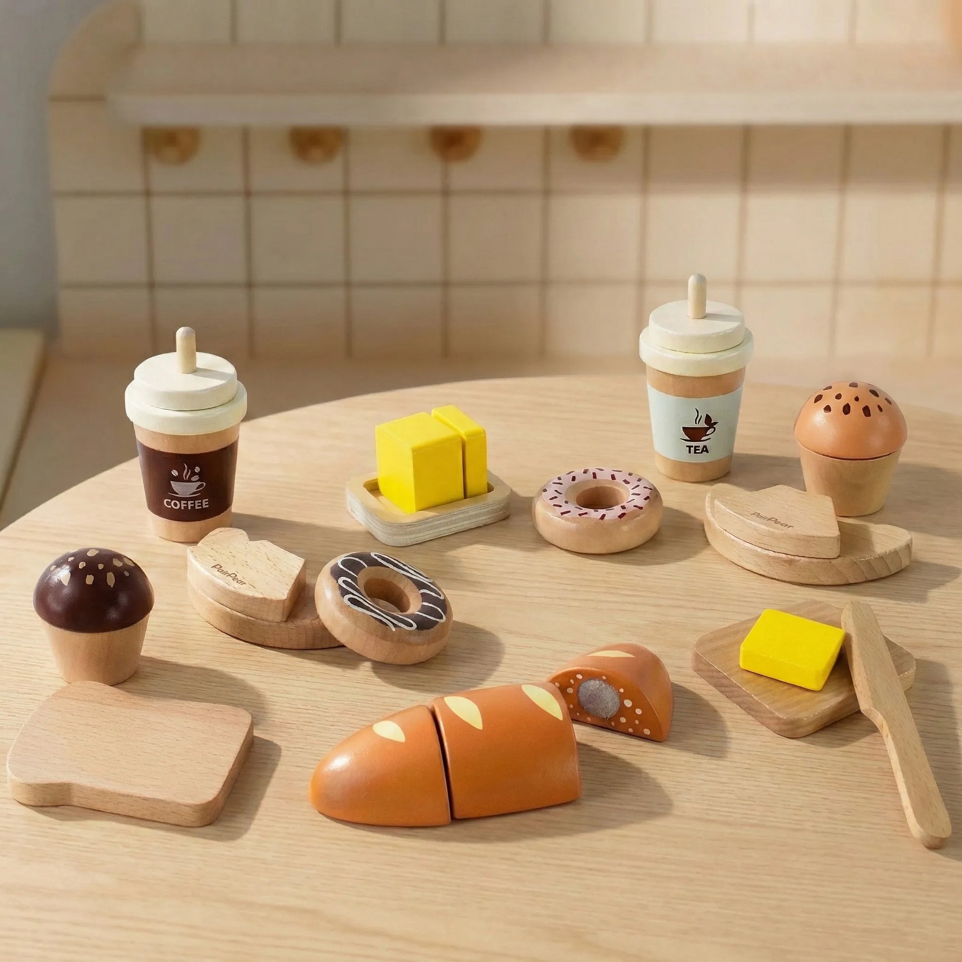 Kids pretend play wooden bakery food on a table. Features toy coffee cups, a cuttable baguette, butter, and pastries in a toy kitchen setting.