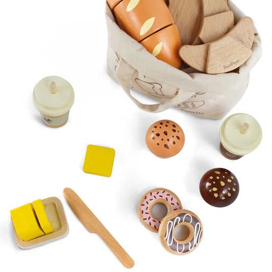 Top-down view of interactive wooden bakery play food. Shows a toy knife ready to cut butter, alongside pretend coffee, donuts, and sliced bread.
