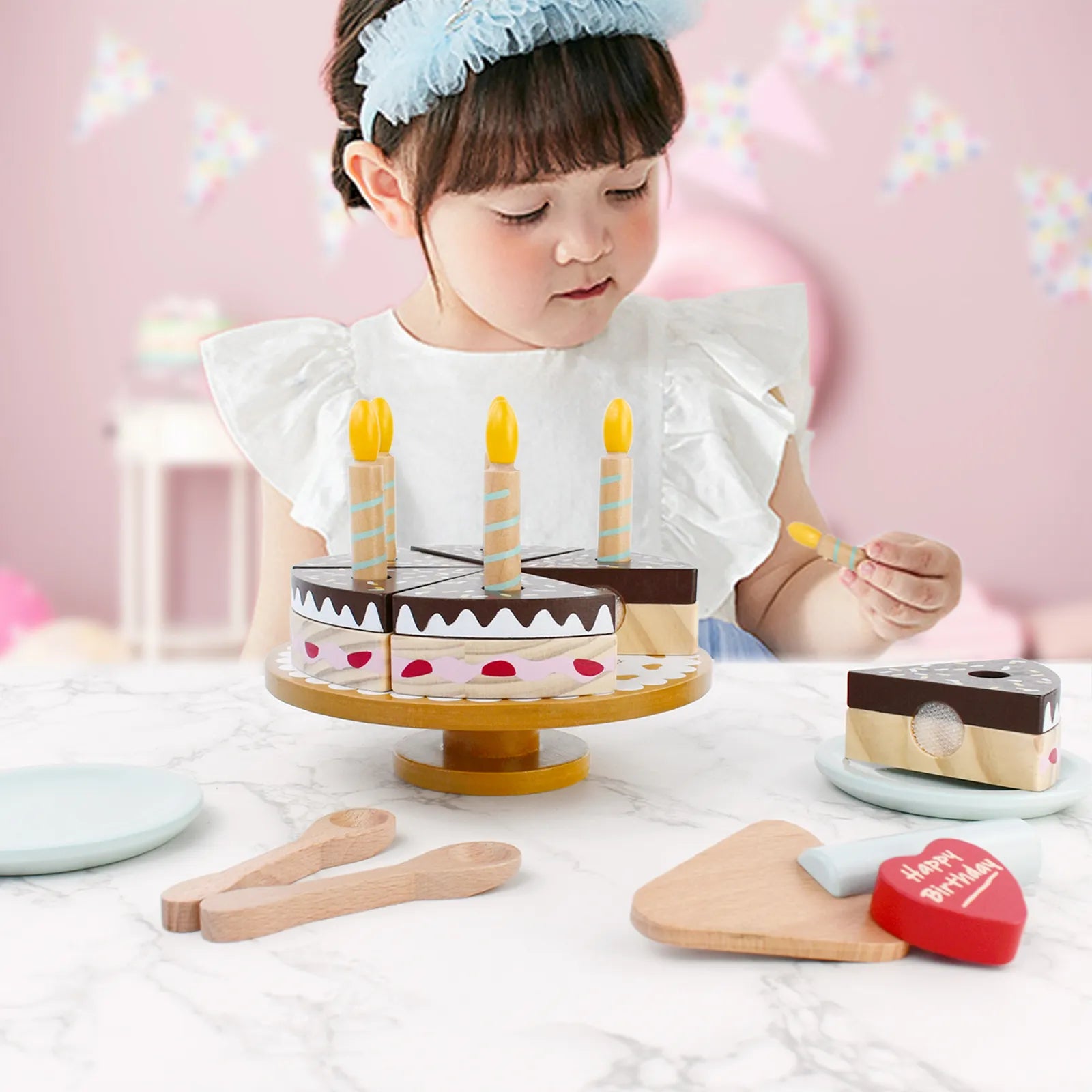 Toddler girl playing with a wooden birthday cake toy. This pretend play food set is a perfect gift for kids to enjoy imaginary birthday parties.