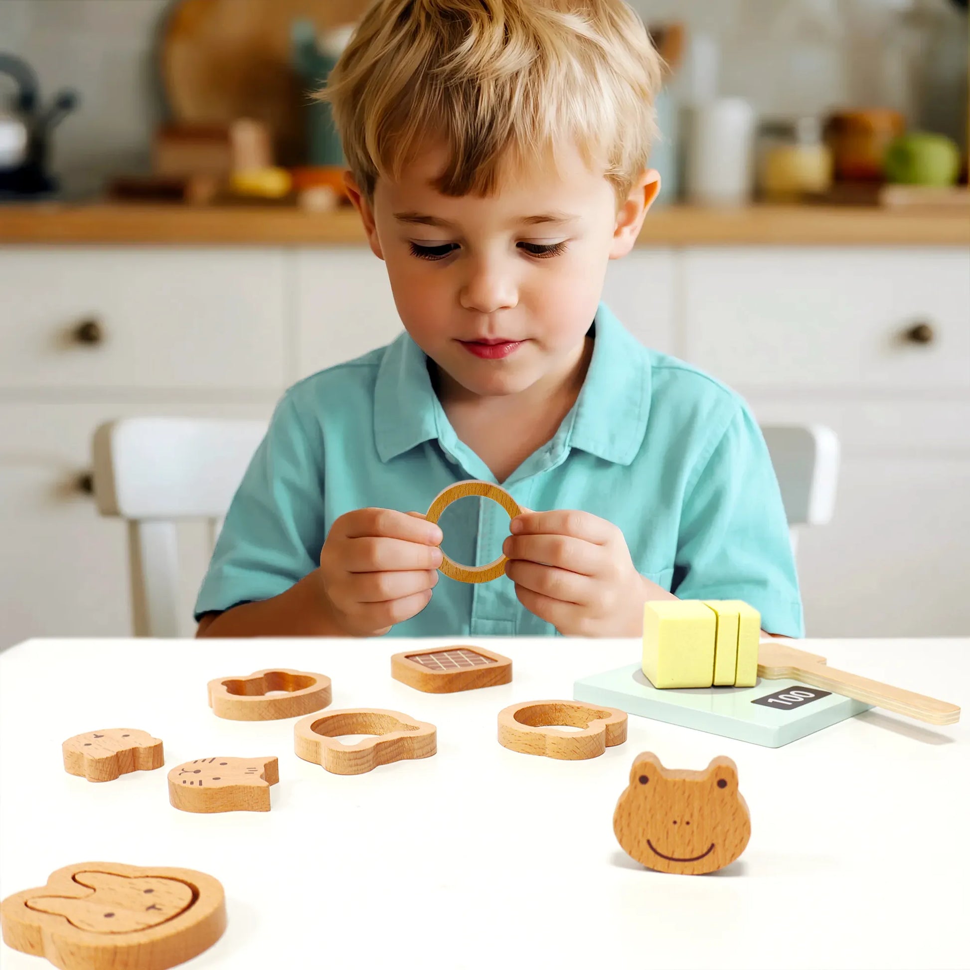 Happy toddler boy playing with a wooden baking set. He is holding a pretend play food cookie, enjoying imaginative play with kitchen accessories.