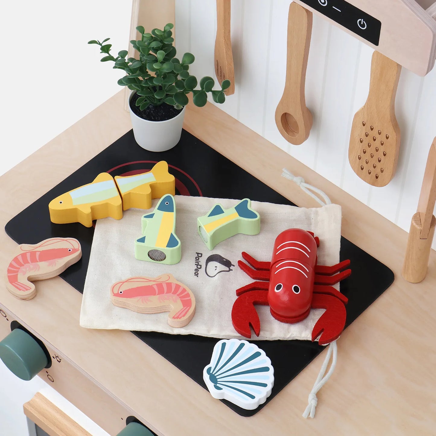 Wooden seafood pretend play toys resting on a toddler's play kitchen stove. Fun cuttable fish, lobster, and shrimp for imaginative cooking games